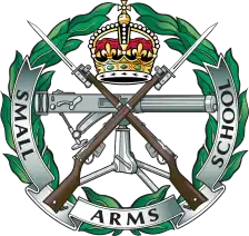 SASC cap badge: crossed rifles over a machine gun in a laurel wreath, with a crown and SMALL ARMS SCHOOL scroll.